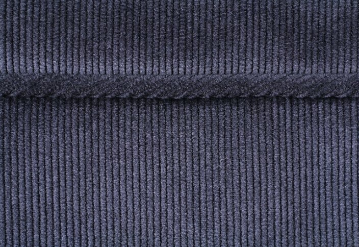 Close-up de tecido corduroy azul escuro com nervuras verticais em relevo, conhecidas como wales.