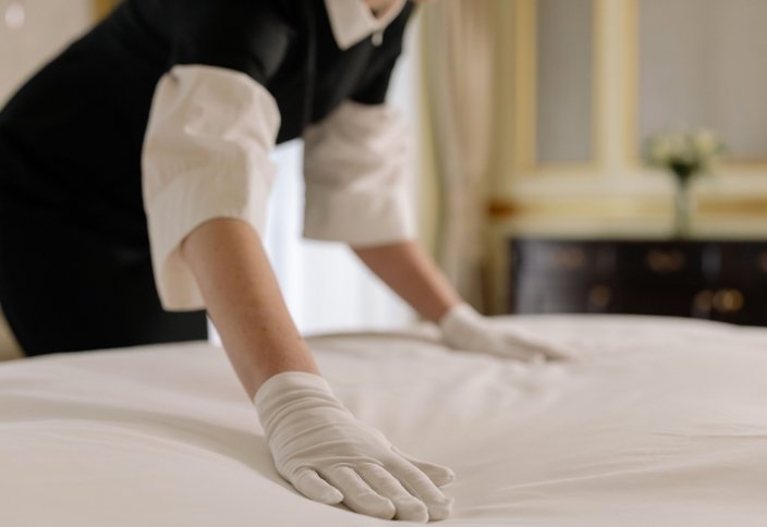 Profissional de hotelaria a preparar roupa de cama resistente para utilização intensiva
